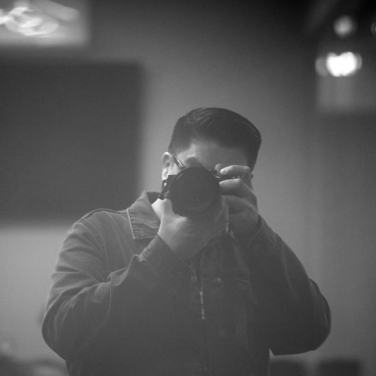 Black and white photo of a man holding a camera up to his face, photographing in an urban setting with city lights